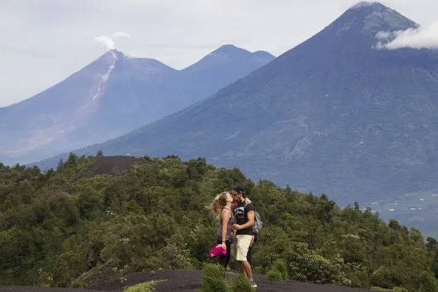 In this June 8, 2018 photo, Aa couple of tourists kiss with the view of the volcanoes, Fuego, left, Acatenango, center, and Agua, right, in the background, from a point in the climb to the Pacaya Volcano, in San Francisco de Sales, Guatemala. Volcano tourism is the life blood of villages like San Francisco de Sales, perched near Pacaya’s peak, and for locals it is a question of learning to live with a generous monster. (Photo by Luis Soto/AP Photo)