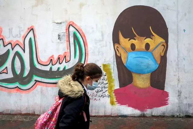 A Palestinians girl walks past a coronavirus awareness mural in Khan Yunis in the southern Gaza Strip, on January 20, 2021. (Photo by Majdi Fathi/NurPhoto via Getty Images)