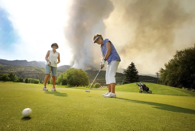 In this Tuesday, June 12, 2018, photograph, Sandy Elliott follows her putt while playing a round of golf with Marlene Gebhardt at Dalton Golf and Country Club with the 416 Fire burning behind them near Durango, Colo. The two ladies are on pre evacuation in Dalton ranch and said we have been looking at the the fire for days and we can't just sit around everyday so they decided to hit the links. (Photo by Jerry McBride/The Durango Herald via AP Photo)