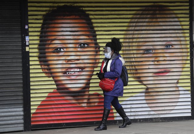 A woman wears protective face coverings as she passes the shutters of a closed shop in West Ealing in London, Thursday, February 25, 2021. It has been announced that further testing of residents in the London Borough of Ealing will be carried out after additional cases of the coronavirus variant first identified in South Africa were detected. (Photo by Kirsty Wigglesworth/AP Photo)