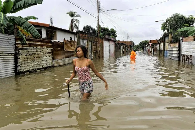 A woman wades through a flooded street while Civil Protection personnel look for people to be evacuated after heavy rains caused by tropical waves affected several communities in the city of Valencia, Carabobo State, Venezuela, on May 30, 2023. (Photo by Juan Carlos Hernandez/AFP Photo)