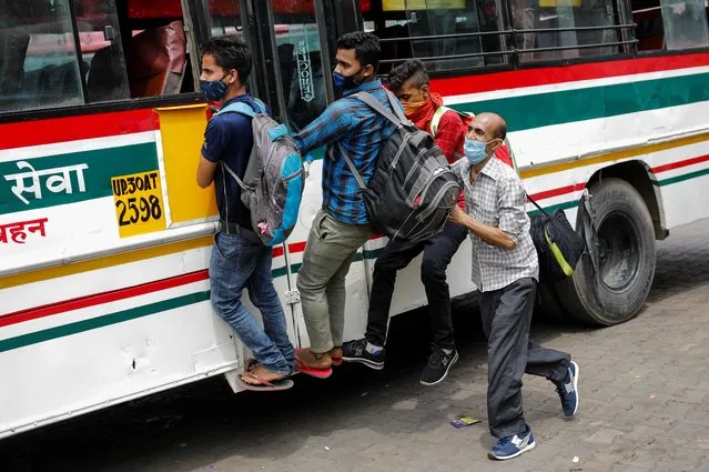 Migrant workers hang on to a door of a moving bus as they return to their villages after Delhi government ordered a six-day lockdown to limit the spread of the coronavirus disease (COVID-19), in Ghaziabad on the outskirts of New Delhi, India, April 20, 2021. (Photo by Adnan Abidi/Reuters)