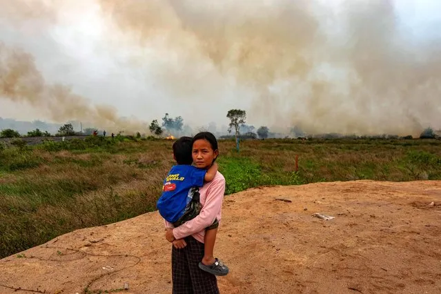 This picture taken on October 4, 2023, shows Poppy, 12, holding her brother as Indonesian firefighters try to extinguish a peatland fire near her house in Palembang, South Sumatra. (Photo by Al Zulkifli/AFP Photo)
