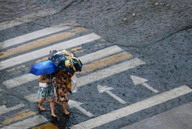 Women walk barefoot across the street during heavy rain in Moscow, Russia on June 28, 2021. (Photo by Evgenia Novozhenina/Reuters)