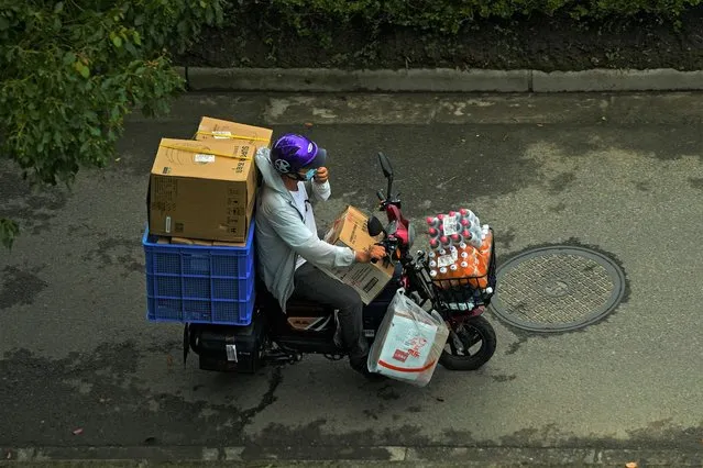 A delivery worker adjusts his face mask to help curb the spread of the coronavirus rides on an electric-powered scooter loaded with parcels and beverages on a street in Shanghai, China, Monday, August 16, 2021. China's retail sales and industrial production growth weakened in July as floods and COVID-19 outbreaks in parts of China disrupted the consumption and supply chain, a government spokesperson said on Monday. (Photo by Andy Wong/AP Photo)