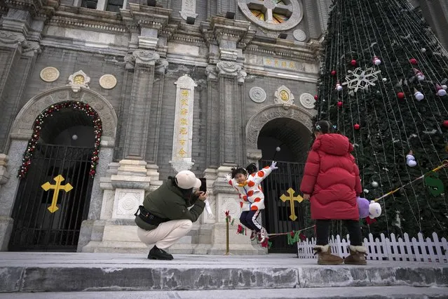 A woman takes a picture of a child jumping near a Christmas tree decorated outside the Wangfujing Church, a Catholic church, on Christmas Eve in Beijing, Sunday, December 24, 2023. Like other western festivals, Christmas is not traditionally celebrated in China, but it has been a common thing among young Chinese in big cities across China. (Photo by Andy Wong/AP Photo)