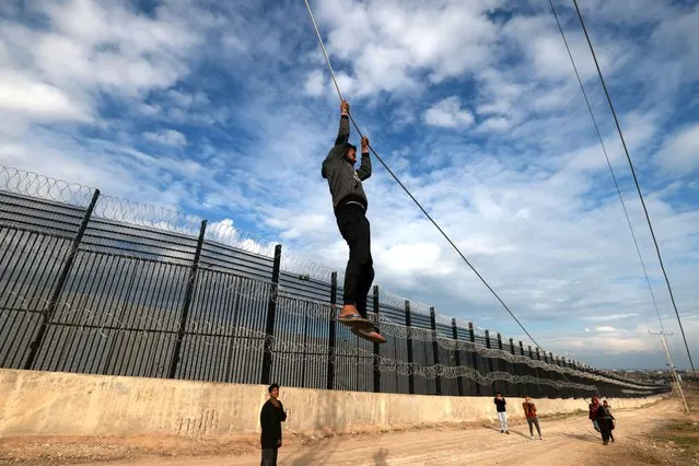 A displaced Palestinian boy hangs on a non functioning electricity cable as he plays near the border fence between Gaza and Egypt, on February 16, 2024 in Rafah, in the southern Gaza Strip, amid the ongoing conflict between Israel and the Palestinian Hamas militant group. Nearly 1.5 million displaced Palestinians are trapped in Rafah – more than half of Gaza's populations – seeking shelter in a sprawling makeshift encampment near the Egyptian border. (Photo by Mohammed Abed/AFP Photo)
