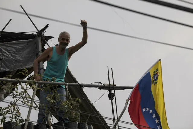 A man holds up his fist to show support for the government of President Nicolas Maduro, from his balcony which overlooks a public square where residents socialize and dance in Caracas, Venezuela, at sunset Saturday, May 11, 2019. (Photo by Rodrigo Abd/AP Photo)
