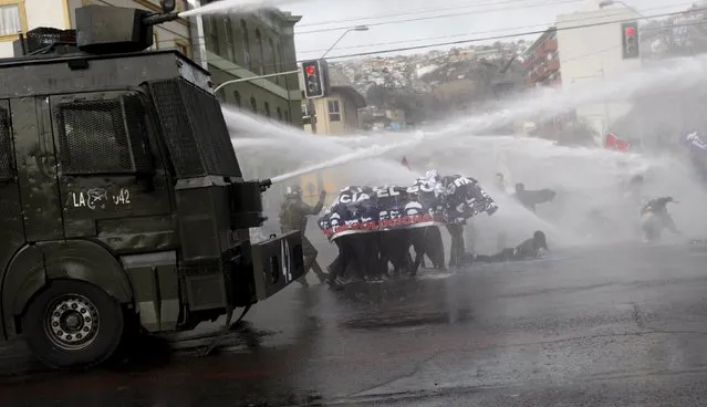 Demonstrators are hit by jets of water released by riot police vehicles during a rally, as Chile's President Michelle Bachelet delivers a speech inside the National Congress, in Valparaiso city, May 21, 2015. (Photo by Carlos Vera/Reuters)