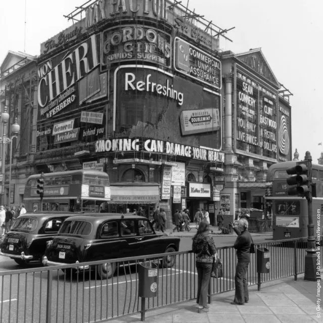 1971: Two girls pointing at the signs in Piccadilly circus, London, which include an advertisement for Wrigley's Chewing gum and a Government health warning about smoking
