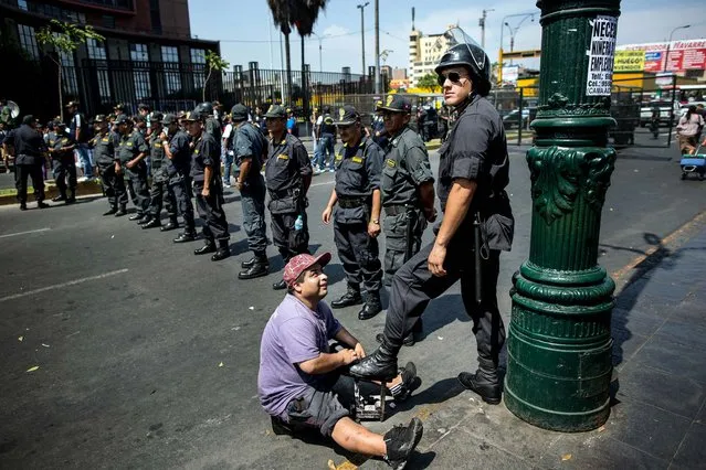 A shoe-shiner polishes the boots of a policeman  standing guard at a protest organized by artisanal and small-scale gold miners in Lima, Peru, on March 24, 2014.The miners marched in the country's capital for the fifth day asking the government to repeal regulations aimed at formalizing informal miners. (Photo by Rodrigo Abd/Associated Press)