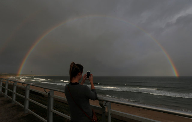 A woman takes a picture of rainbow appearing off the coast of Sydney's Wanda Beach in Australia, February 25, 2017 as the setting sun illuminates a passing rain shower. (Photo by Jason Reed/Reuters)