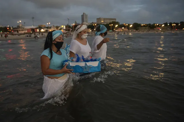 Locals carry an offering during a ritual for the African sea goddess Yemanja at Ramirez Beach in Montevideo, Uruguay, Tuesday, February 2, 2021. Worshippers showed up at Ramirez Beach on Yemanja's feast day, bearing candles, flowers, and fruit though the authorities had asked them not to go because of the COVID-19 pandemic. (Photo by Matilde Campodonico/AP Photo)
