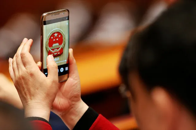 An attendee takes a picture of China's national emblem inside the Great Hall of the People during the third plenary session of the National People's Congress (NPC) in Beijing, China, March 12, 2017. (Photo by Tyrone Siu/Reuters)