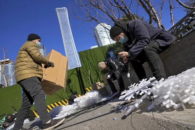 Workers wearing face masks install snowflake-shaped lights near the Central Business District in Beijing, Monday, January 17, 2022. (Photo by Andy Wong/AP Photo)
