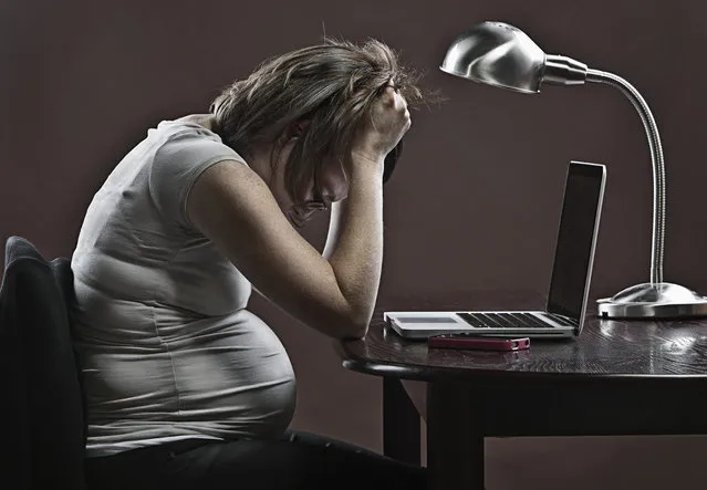 Stressed pregnant business woman sitting at desk in front of laptop. (Photo by Justin Paget/Getty Images)