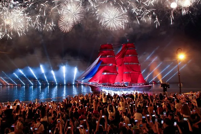 Spectators watch fireworks exploding in the sky and the brig “Rossiya” (Russia) with scarlet sails floating along the Neva River during festivities in honour of school graduates in Saint Petersburg, Russia on June 26, 2021. (Photo by Anton Vaganov/Reuters)