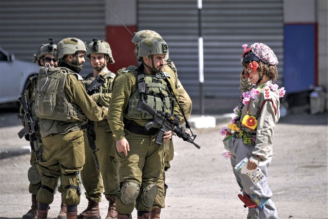 An Israeli activist dressed as a clown salutes to a group of Israeli soldiers during a solidarity rally by Israeli left-wing activists in the West Bank town of Hawara which was set ablaze by radical Jewish settlers earlier this week, Friday, March 3, 2023. On Monday scores of Israeli settlers have gone on a violent rampage in the northern West Bank town of Hawara, setting cars and homes on fire after two settlers were killed by a Palestinian gunman. (Photo by Majdi Mohammed/AP Photo)