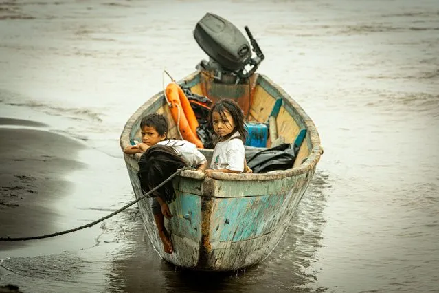 Children remain on a boat, after crude reached the Coca river due to an oil spill, in Puerto Maderos, Sucumbios province, Ecuador, on February 1, 2022. An oil spill caused by a ruptured pipeline in Ecuador's Amazon region leaked almost 6,300 barrels into an environmental reserve, according to information provided Wednesday by the company that owns the conduit. (Photo by Cristina Vega Rhor/AFP Photo)