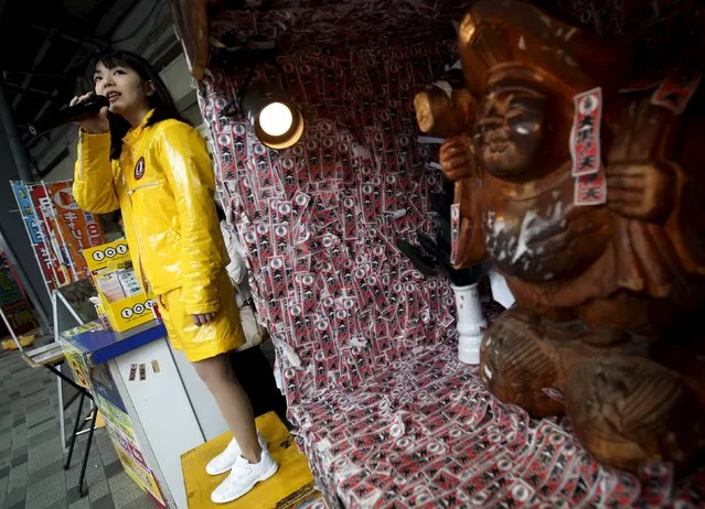 A woman holding a microphone entices shoppers to buy lotteries next to a wooden figure of Daikoku-sama, the god presiding over food and wealth, at the Tokyo's Ginza shopping district, Japan, May 19, 2015. (Photo by Yuya Shino/Reuters)
