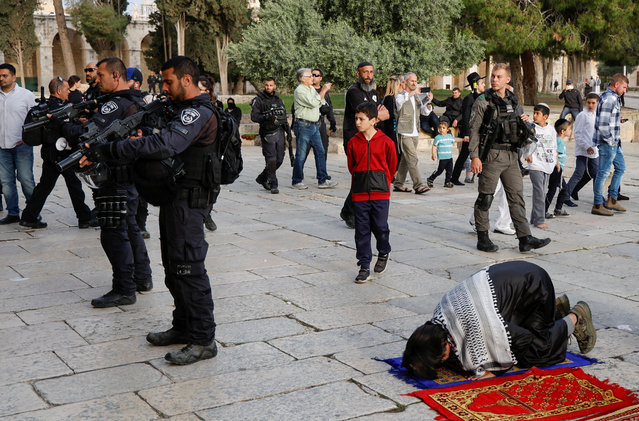 Members of the Israeli security forces stand near Palestinian people praying at the Al-Aqsa compound, also known to Jews as the Temple Mount, while tension arises during clashes in Jerusalem's Old City on April 9, 2023. (Photo by Ammar Awad/Reuters)