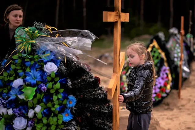 Darya Piven, 33, looks as her daughter Zlata, 6, as she visits the graves of her parents Nadiya Myakushko, 69, and Volodymyr Cherednichenko, 75, who were killed by Russian army in Irpin on March 24, in Irpin, on the outskirts of Kyiv, Monday, April 25, 2022. (Photo by Emilio Morenatti/AP Photo)