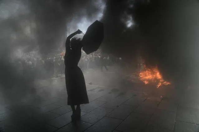 A demonstrator holds onto an umbrella surrounded by clouds of smoke during clashes with demonstrators protesting the government’s agreement with the International Monetary Fund to refinance some $45 billion in debt, as legislators prepare to vote on a law to ratify the agreement, in Buenos Aires, Argentina, Thursday, March 10, 2022. (Photo by Rodrigo Abd/AP Photo)