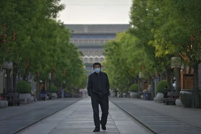 A man wearing a face mask to help protect from the coronavirus walks along a quiet Qianmen shopping street on Thursday, April 28, 2022, in Beijing. Beijing is closing all city schools in a further tightening of COVID-19 restrictions, as China's capital seeks to prevent a wider outbreak. (Photo by Andy Wong/AP Photo)