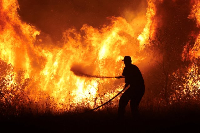 A firefighter tries to extinguish a wildfire burning at the industrial zone of the city of Volos, in central Greece on July 26, 2023. (Photo by Alexandros Avramidis/Reuters)