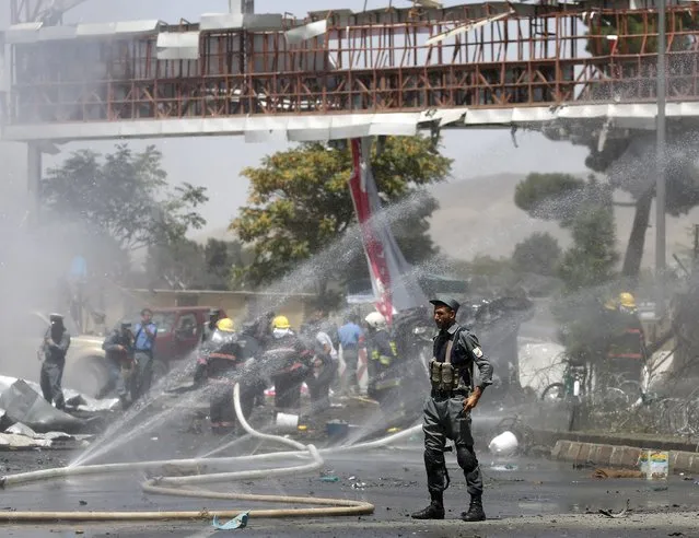 A policeman stands guard as fire is being extinguished after a car bomb at the entrance gate to the Kabul airport in Afghanistan August 10, 2015. (Photo by Ahmad Masood/Reuters)