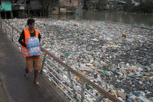 A man carrying water bottles crosses a bridge next to accumulated garbage floating on the Negro River, which has a rising water level due to rain, in Manaus, Amazonas state, Brazil, Monday, June 6, 2022. About 35 tons of garbage are removed daily from the water in Manaus, according to the city. (Photo by Edmar Barros/AP Photo)