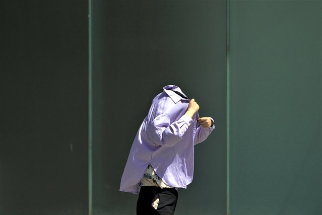 A woman uses a long-sleeve shirt to shield from the sun as she walks at an outdoor shopping mall on a sweltering day in Beijing, Thursday, July 6, 2023. Employers in Beijing were ordered Thursday by the government to stop outdoor work after scorching summer heat in the Chinese capital was forecast to reach 40 degrees centigrade (104 Fahrenheit). (Photo by Andy Wong/AP Photo)