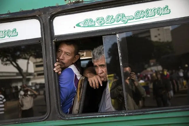In this November 16, 2019 photo, commuters look at a small group anti-government demonstrators from a passing bus in Maracaibo, Venezuela. (Photo by Rodrigo Abd/AP Photo)