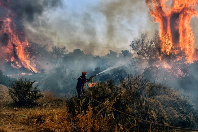 A fireman douses flames on a wildfire at Panorama settlement near Agioi Theodori, some 70 kms west of Athens on July 18, 2023. Europe braced for new high temperatures on July 18, 2023, under a relentless heatwave and wildfires that have scorched swathes of the Northern Hemisphere, forcing the evacuation of 1,200 children close to a Greek seaside resort. Health authorities have sounded alarms from North America to Europe and Asia, urging people to stay hydrated and shelter from the burning sun, in a stark reminder of the effects of global warming. (Photo by Valerie Gache/AFP Photo)