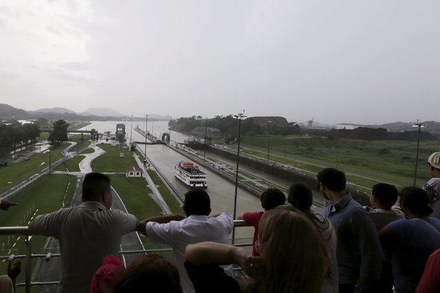 Visitors look at a boat navigating through the Miraflores locks of the Panama Canal, during the 101st anniversary of the waterway's opening in Panama City August 15, 2015. The Panama Canal was inaugurated on August 15, 1914. (Photo by Carlos Jasso/Reuters)