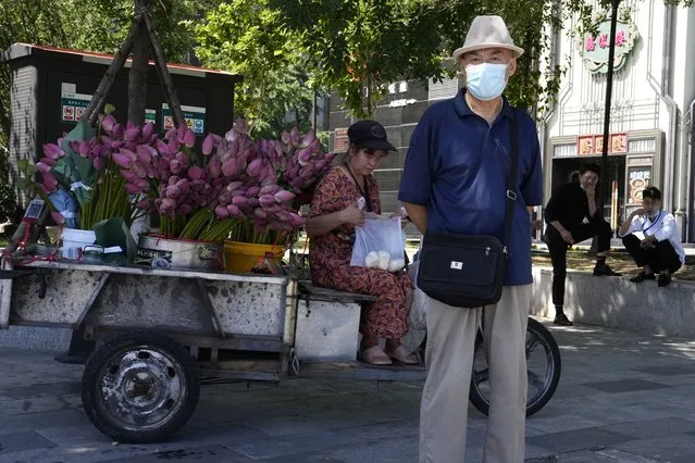 An elderly man wearing a mask stands near a street vendor selling lotus flowers, Thursday, July 7, 2022, in Beijing. (Photo by Ng Han Guan/AP Photo)