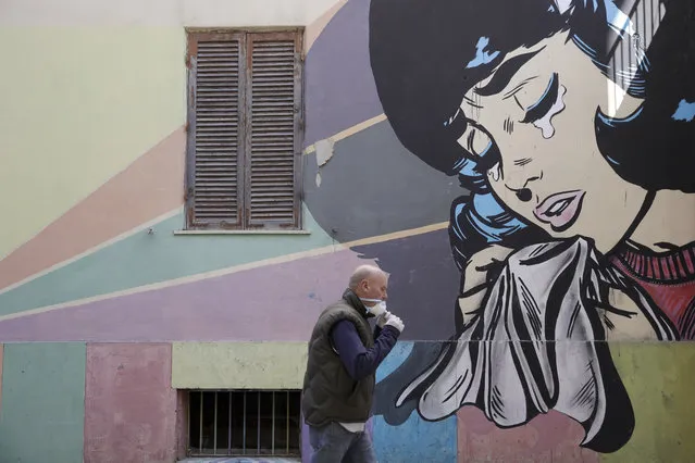 A man adjusts his face mask as he walks past a mural of a crying woman in Rome's Trullo neighborhood, Monday, March 16, 2020. The vast majority of people recover from the new coronavirus. According to the World  Health Organization, most people recover in about two to six weeks, depending on the severity of the illness. (Photo by Alessandra Tarantino/AP Photo)