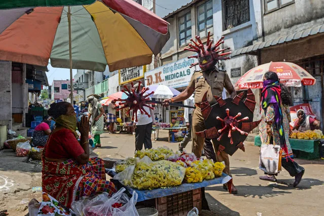 A policeman (R) wearing a coronavirus-themed outfit composed of helmet, mace and shield, gestures towards a vendor at a market to raise awareness about social distancing, during a government-imposed nationwide lockdown as a preventive measure against the COVID-19 coronavirus, in Chennai on April 2, 2020. (Photo by Arun Sankar/AFP Photo)