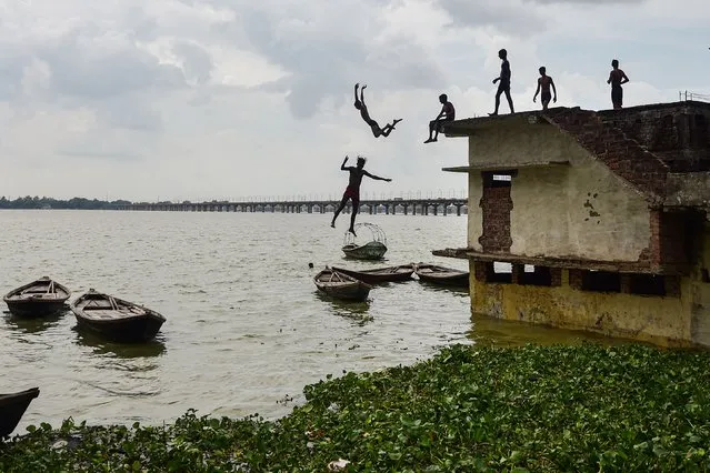 Youths jump from a partially submerged home into the overflown Ganges River in the Jushi area in Allahabad on August 19, 2022, after water level rose following monsoon rains. (Photo by Sanjay Kanojia/AFP Photo)