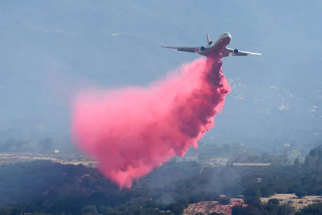 A DC-10 air tanker sprays fire retardant near homes in Hesperia, Calif, near a wildfire on Sunday, August 7, 2016. (Photo by David Pardo/The Daily Press via AP Photo)
