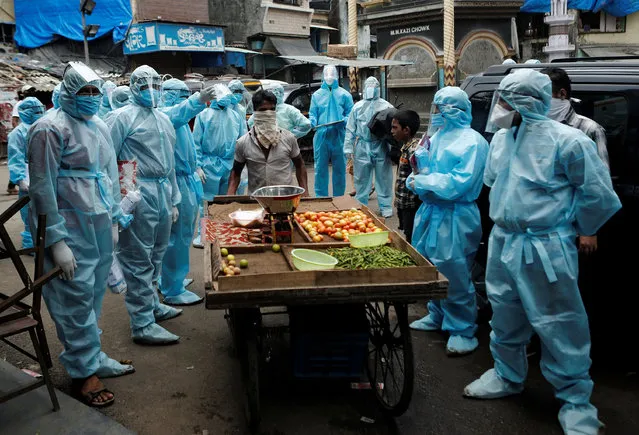 A vegetable vendor pushes his handcart past healthcare workers wearing personal protective equipment (PPE) after a check up for the coronavirus disease (COVID-19) at a slum in Mumbai, India, June 14, 2020. (Photo by Francis Mascarenhas/Reuters)