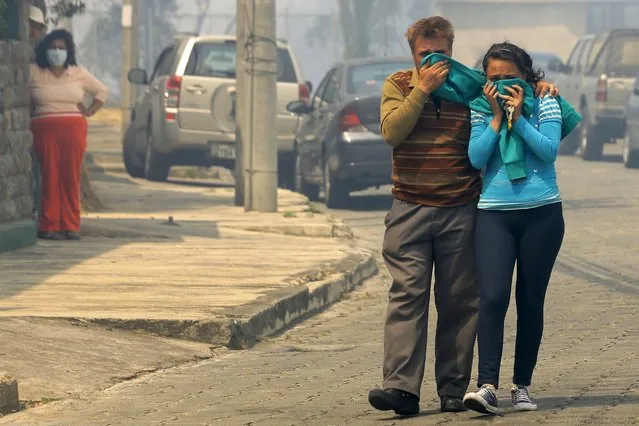 A man and his daughter cover their faces as they leave their house during a forest fire in the hillsides around Quito, on September 15, 2015. Ecuador asked Brazil, Chile, Colombia, Peru and Venezuela for help Tuesday to control a wave of forest fires manly in Quito, where three firefighters were killed and 50 people were evacuated. (Photo by Juan Cevallos/AFP Photo)