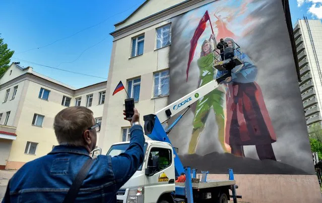 Street artist Alexander Sazhin paints a mural as part of a joint project by the Tavrida Art Cluster and the Youth, Sport and Tourism Ministry of the Donetsk People's Republic on May 20, 2022. The 82sqm mural on the facade of Specialised School No 47 features the Red Banner Grandma, a young woman wearing a Red Army uniform, and the Motherland Calls monument. (Photo by Nikolai Trishin/TASS)