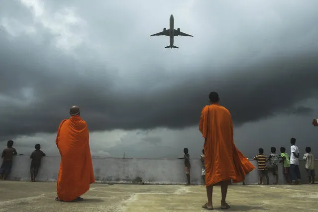 Buddhists monks and children look out from the rooftop at a Buddhist mission hostel and school for underprivileged children as an international passenger flight takes off at the Netaji Subhash Chandra Bose International Airport as the authorities eased restrictions imposed as a preventive measure against the spread of the COVID-19 coronavirus, in Kolkata on July 5, 2020. (Photo by Dibyangshu Sarkar/AFP Photo)