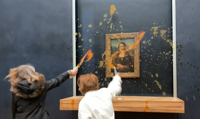 This image grab taken from AFPTV footage shows two environmental activists from the collective dubbed “Riposte Alimentaire” (Food Retaliation) hurling soup at Leonardo Da Vinci's “Mona Lisa” (La Joconde) painting, at the Louvre museum in Paris, on January 28, 2024. Two protesters on January 38, 2024 hurled soup at the bullet-proof glass protecting Leonardo da Vinci's "Mona Lisa" in Paris, demanding the right to “healthy and sustainable food”, an AFP journalist said. It is the latest attack on the masterpiece in the French capital's Louvre museum, after someone threw a custard pie at it in May 2022, but it's thick glass casing ensured it came to no harm. (Photo by David Cantiniaux/AFPTV via AFP Photo)