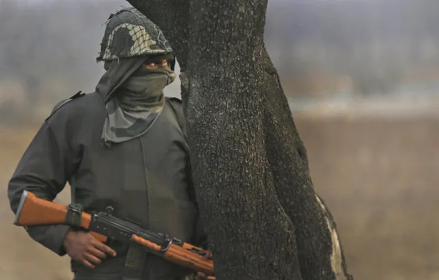 An Indian paramilitary force soldier takes cover behind a tree at the site where suspected rebels stormed a paramilitary camp at southern Lethpora village, Indian controlled Kashmir, Monday, December 31, 2017. (Photo by Mukhtar Khan/AP Photo)