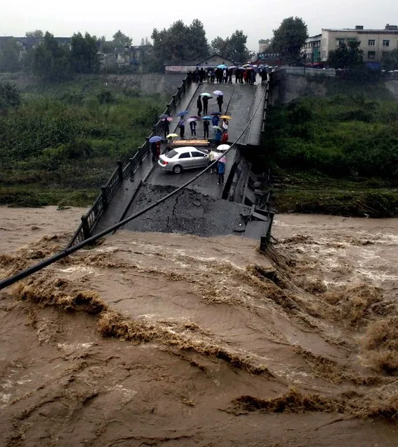 A car sits precariously on a bridge after it collapsed due to rising floodwaters in Huaiyuan, in southwest China's Sichuan province. (Photo by AFP Photo)