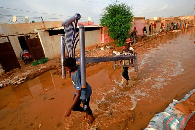 Sudanese youth carry a bed frame as they make their way through a flooded street in alqamayir area in the capital's twin city of Omdurman, on August 26, 2020. (Photo by Ashraf Shazly/AFP Photo)