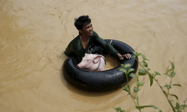 A man holds a pig on a float to cross a flooded road amidst a strong current in Sta Rosa, Nueva Ecija in northern Philippines October 19, 2015, after it was hit by Typhoon Koppu. (Photo by Erik De Castro/Reuters)