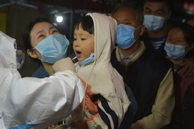 A medical staff takes a swab from a child as residents wearing face masks to help curb the spread of the coronavirus line up for the COVID-19 test near the residential area in Qingdao in east China's Shandong province on Monday, October 12, 2020. Authorities in the eastern Chinese port city of Qingdao said Tuesday that they have completed coronavirus tests on more than 3 million people following the country's first reported local outbreak of the virus in nearly two months. (Photo by Chinatopix via AP Photo)
